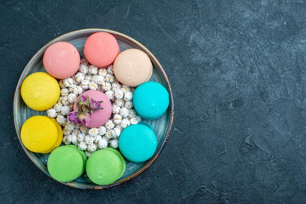 Vue de dessus de délicieux macarons français avec des bonbons à l'intérieur du plateau sur l'espace sombre