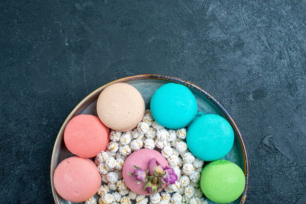 Vue de dessus de délicieux macarons français avec des bonbons à l'intérieur du plateau sur l'espace sombre