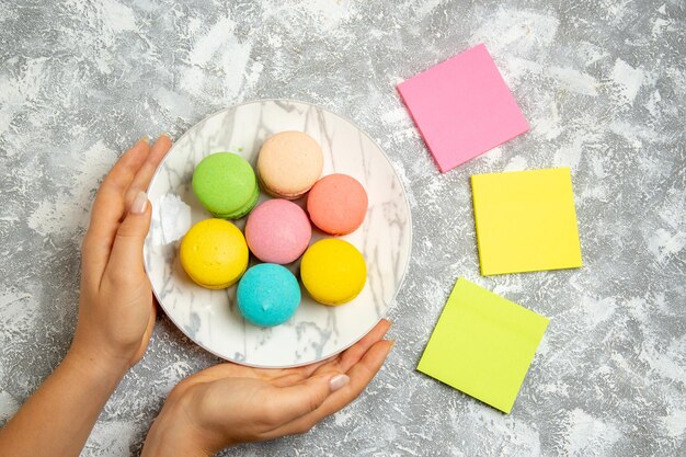 Vue de dessus de délicieux macarons français gâteaux colorés à l'intérieur de la plaque sur une surface blanche