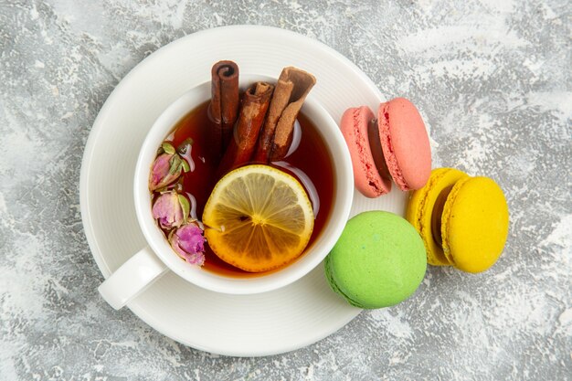 Vue de dessus de délicieux macarons français gâteaux colorés avec une tasse de thé sur une surface blanche