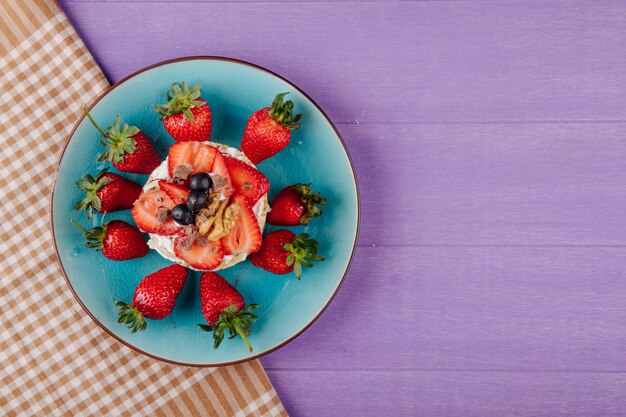 Vue de dessus de délicieux pain croustillant aux bleuets mûrs, fraises et noix avec de la crème sure sur une plaque en céramique sur fond de bois violet avec copie espace