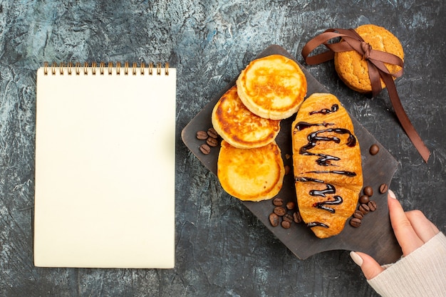 Vue de dessus d'un délicieux petit-déjeuner avec des crêpes et des biscuits empilés croissants et un cahier sur une surface sombre