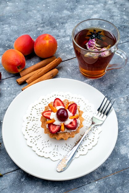 Une vue de dessus délicieux petit gâteau avec de la crème et des fruits frais tranchés avec du thé à la cannelle sur le bureau gris-bleu thé biscuit aux fruits