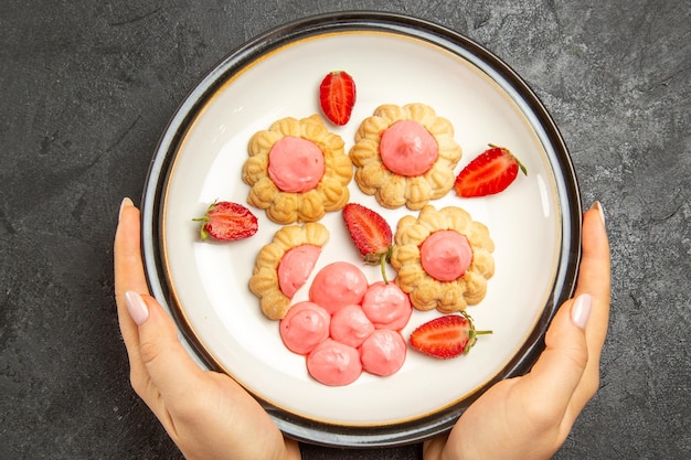 Vue de dessus de délicieux petits biscuits avec de la crème rose à l'intérieur de la plaque sur une surface gris foncé