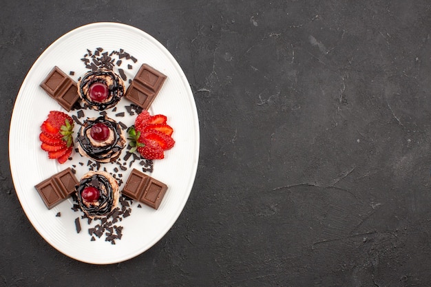 Vue de dessus de délicieux petits gâteaux avec des barres de chocolat et des fraises sur fond sombre tarte au gâteau au cacao thé sucré