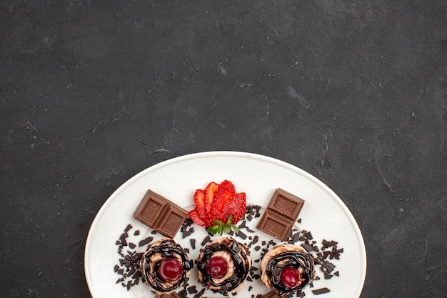 Vue de dessus de délicieux petits gâteaux avec des barres de chocolat et des fraises sur fond sombre tarte gâteau au chocolat et au cacao thé sucré