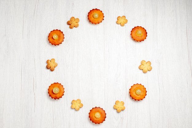 Vue de dessus de délicieux petits gâteaux bordés de biscuits sur un bureau blanc dessert biscuit gâteau au thé tarte biscuit sucré