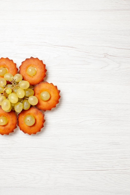 Vue de dessus de délicieux petits gâteaux bordés de raisins sur un bureau blanc tarte au thé gâteau dessert sucré biscuit