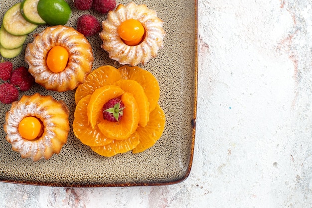 Vue de dessus de délicieux petits gâteaux avec des fruits tranchés sur blanc