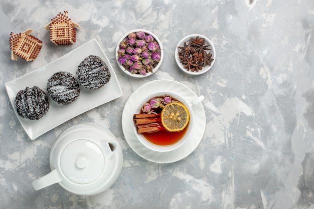 Vue de dessus de délicieux petits gâteaux avec glaçage et tasse de thé sur un bureau blanc gâteau biscuit thé cuire tarte sucrée au sucre