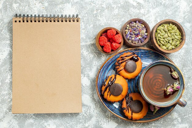 Vue de dessus de délicieux petits gâteaux avec une tasse de thé sur un sol blanc clair gâteau biscuit biscuit dessert thé sucré