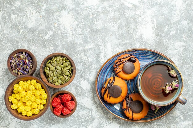 Vue de dessus de délicieux petits gâteaux avec une tasse de thé sur une surface blanche claire gâteau biscuit biscuit dessert thé sucré