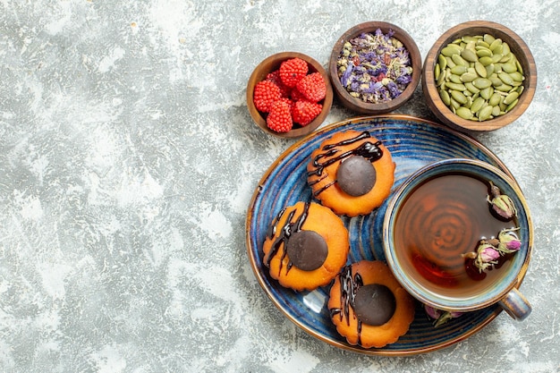 Vue de dessus de délicieux petits gâteaux avec une tasse de thé sur une surface blanche claire gâteau biscuit biscuit dessert thé sucré