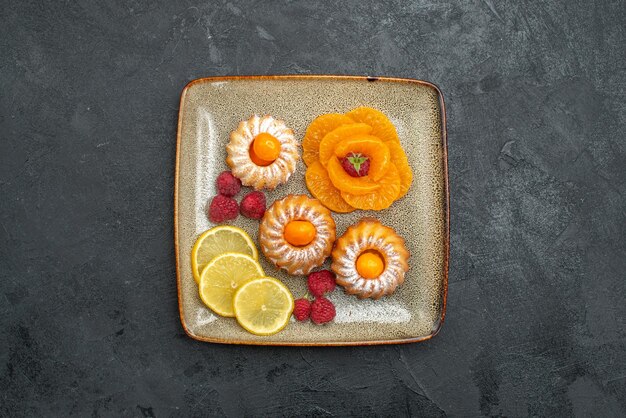 Vue de dessus de délicieux petits gâteaux avec des tranches de citron et des mandarines sur fond sombre biscuit aux fruits biscuit au thé sucré