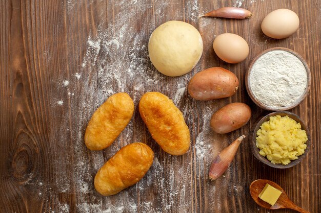 Vue de dessus de délicieux petits pains aux pommes de terre avec des ingrédients sur un bureau en bois marron, un four à gâteau à tarte à gâteau