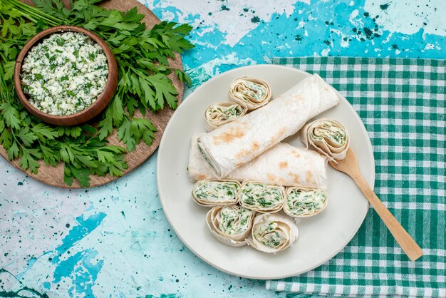 Vue de dessus de délicieux petits pains de légumes entiers et tranchés avec des verts et de la salade sur la table bleue de la couleur végétale du rouleau de repas alimentaire