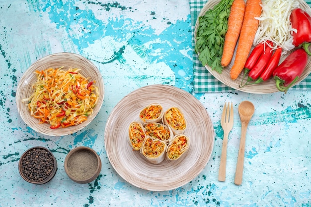 Vue de dessus de délicieux petits pains de légumes tranchés avec salade fraîche et légumes sur un bureau bleu vif, petit pain de salade de repas de légumes