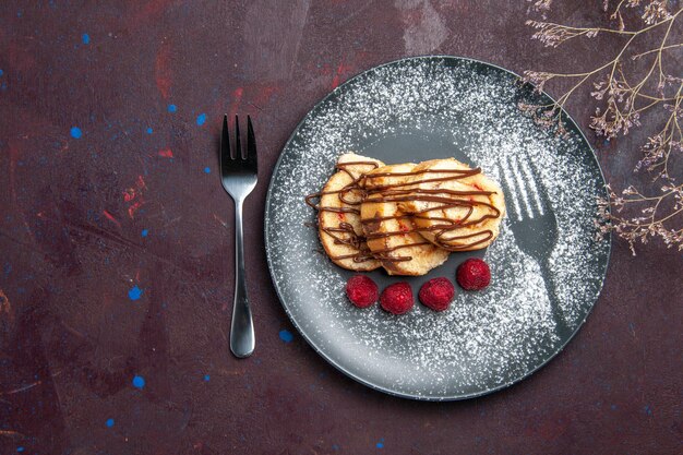 Vue de dessus de délicieux petits pains sucrés en tranches de gâteau pour le thé à l'intérieur de la plaque sur le fond sombre rouleau biscuit tarte sucrée dessert au thé