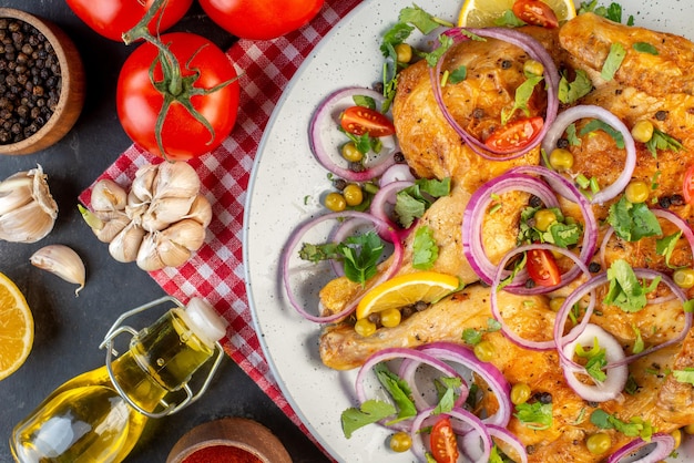 Vue de dessus d'un délicieux plat de poulet frit avec diverses épices et aliments tomates avec tiges poivre oignons ails bouteille d'huile tombée sur fond de couleur sombre