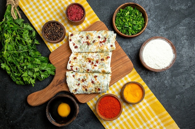 Vue de dessus de délicieux qutabs de tranches de pâte cuites avec des légumes verts et différents assaisonnements sur un espace gris