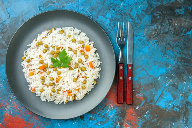 Vue de dessus d'un délicieux repas de riz avec carotte pisum servi avec du vert sur une assiette de couverts sur fond de couleur mélangée avec espace libre