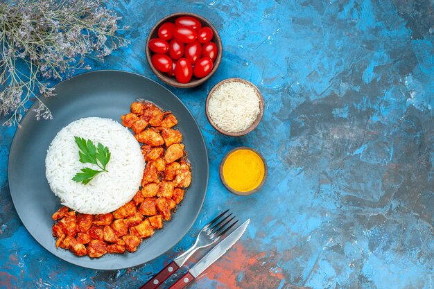 Vue de dessus d'un délicieux repas de riz avec des couverts de poulet vert et tomate mis des tomates à l'ail sel sur le côté droit sur la table bleue