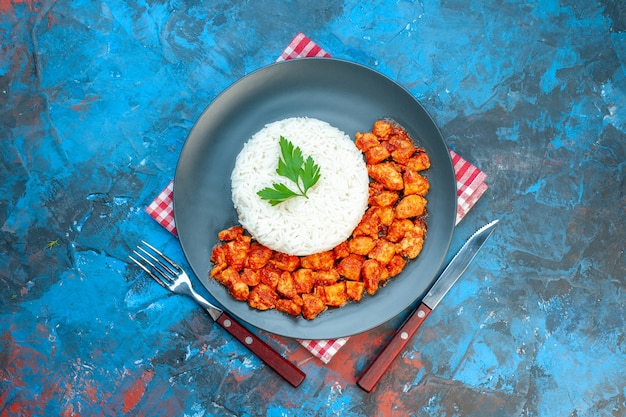 Vue de dessus d'un délicieux repas de riz avec du poulet vert et tomate sur une serviette rouge à côté de couverts sur une table bleue