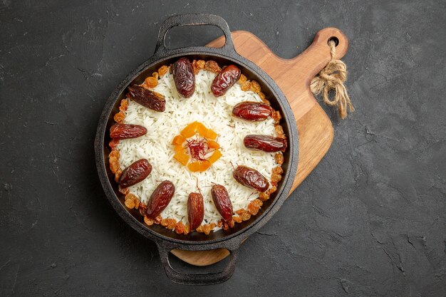 Vue de dessus délicieux repas de riz plov cuit avec khurma et raisins secs sur une surface sombre plat de cuisson de riz plov repas