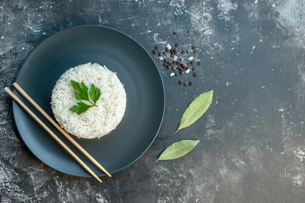 Vue de dessus d'un délicieux repas de riz servi avec du vert et des baguettes sur une plaque noire de poivrons sur le côté droit sur fond sombre