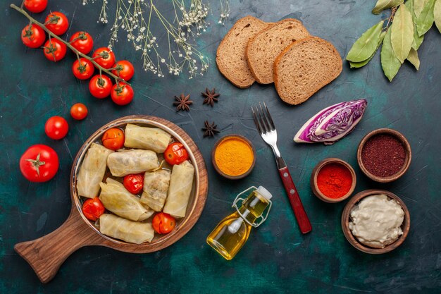 Vue de dessus délicieux repas de viande roulé à l'intérieur du chou avec du pain à l'huile et des tomates fraîches sur un bureau bleu foncé viande alimentaire dîner calorie plat de légumes cuisson
