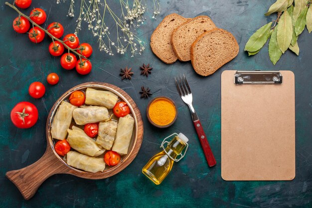 Vue de dessus délicieux repas de viande roulé à l'intérieur du chou avec du pain à l'huile et des tomates fraîches sur un bureau bleu foncé viande nourriture dîner plat de légumes cuisson
