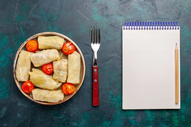 Vue de dessus délicieux repas de viande roulé à l'intérieur du chou avec des tomates et bloc-notes sur le bureau bleu foncé viande nourriture dîner calories légumes cuisson