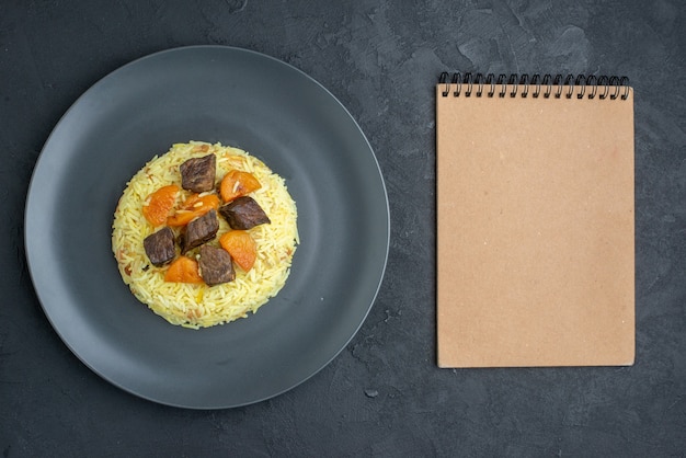 Vue de dessus délicieux riz cuit pilaf avec abricots secs et tranches de viande à l'intérieur de la plaque sur une surface sombre