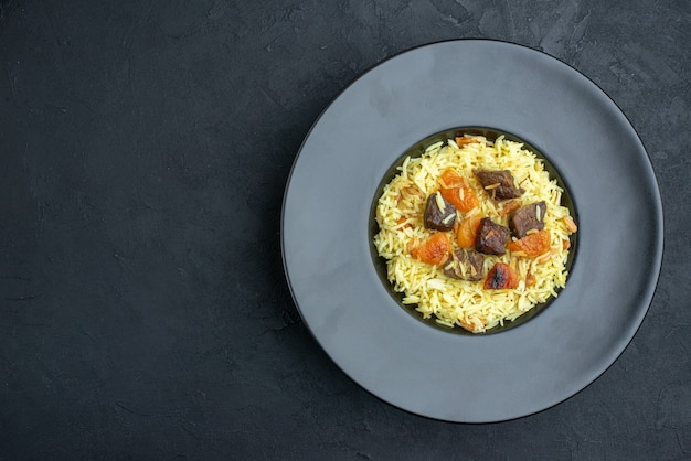 Vue de dessus délicieux riz cuit pilaf avec abricots secs et tranches de viande à l'intérieur de la plaque sur une surface sombre