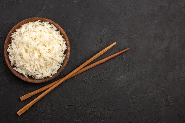 Vue de dessus délicieux riz cuit simple riz savoureux à l'intérieur d'une assiette brune sur l'espace sombre