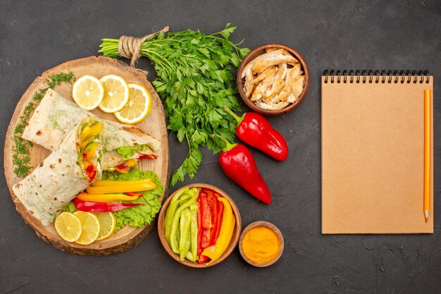 Vue de dessus d'un délicieux sandwich au poulet tranché shaurma avec des tranches de citron et des verts sur l'obscurité