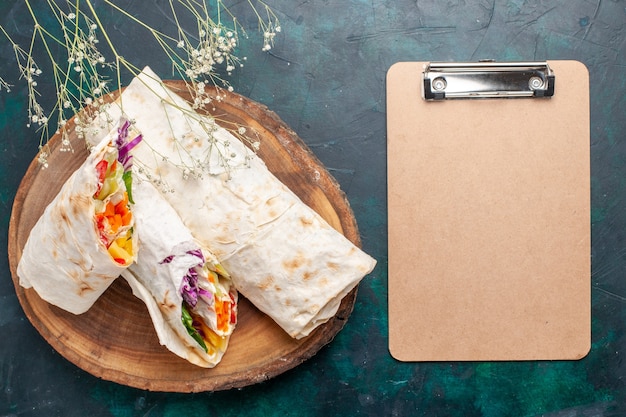 Vue de dessus délicieux sandwich à la viande fait de viande grillée à la broche en tranches avec bloc-notes sur le bureau bleu foncé burger repas de viande déjeuner déjeuner sandwich