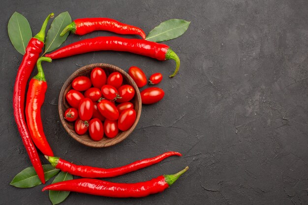 Vue de dessus demi-cercle de piments rouges et de feuilles de laurier et un bol de tomates cerises sur le côté gauche de la table noire