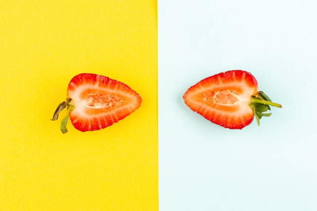 Vue de dessus demi-fraises coupées moelleuses juteuses sur le fond jaune-bleu