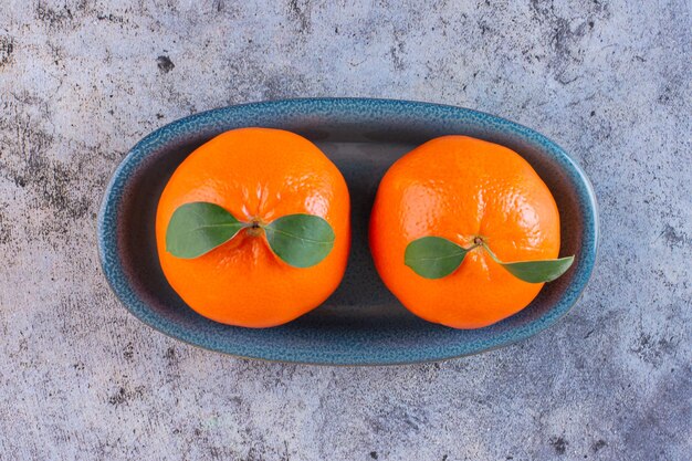 Vue De Dessus De Deux Mandarines Fraîches Avec Des Feuilles Sur Une Plaque En Bois Sur Fond Gris.