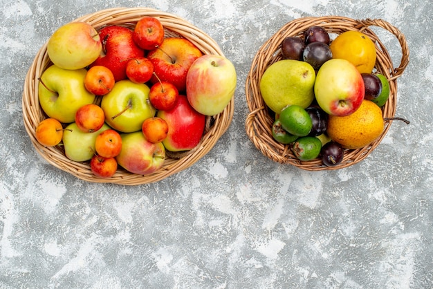 Vue de dessus deux paniers en osier en plastique avec pommes rouges et jaunes et prunes poires feykhoas et kaki sur la table grise