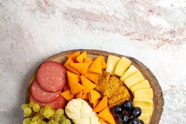 Vue de dessus différentes collations cips saucisses fromage et raisins frais sur sol blanc repas alimentaire collation fruit fromage