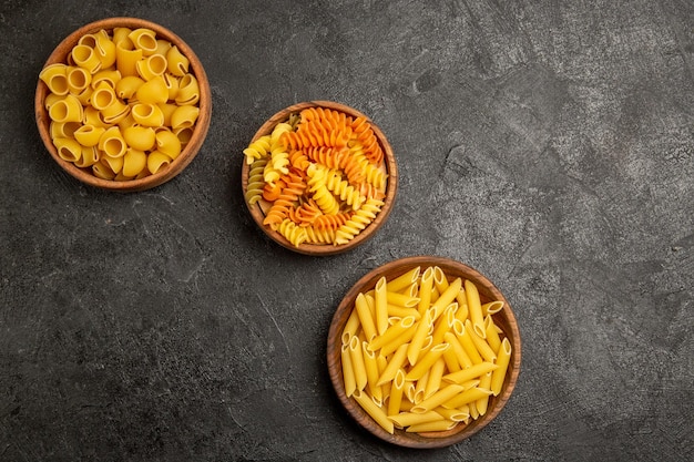 Vue de dessus de différentes compositions de pâtes produit brut à l'intérieur des assiettes sur la cuisson des repas de pâte crue de pâtes grises