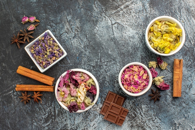 Vue de dessus de différentes fleurs sèches et cannelles et barre de chocolat sur fond gris