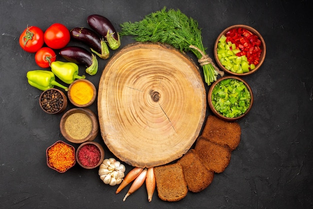 Vue de dessus différents assaisonnements avec des légumes verts et des miches de pain noir sur fond sombre assaisonnements pour salades pain diététique