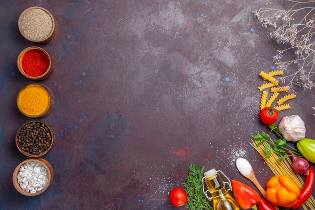 Vue de dessus différents assaisonnements avec des pâtes crues sur fond sombre produit aliments crus salade santé régime