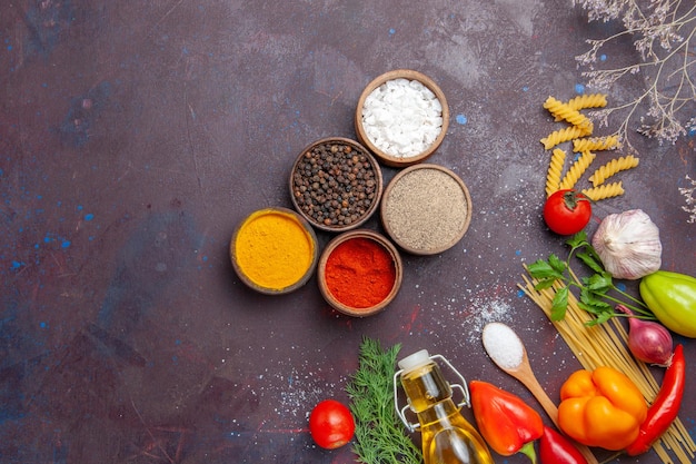 Vue de dessus différents assaisonnements avec des pâtes crues sur fond sombre salade d'aliments crus régime santé pâtes