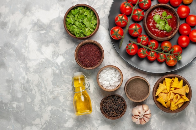 Photo gratuite vue de dessus différents assaisonnements avec des tomates cerises et de l'huile sur un bureau blanc