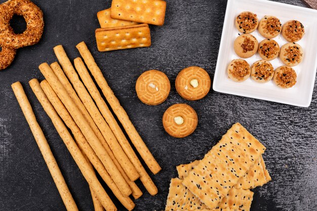 Vue de dessus différents biscuits et bâtonnets de pain sur une surface sombre