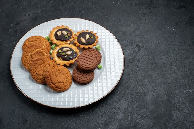 Vue de dessus différents biscuits biscuits sucrés et délicieux sur une surface gris foncé